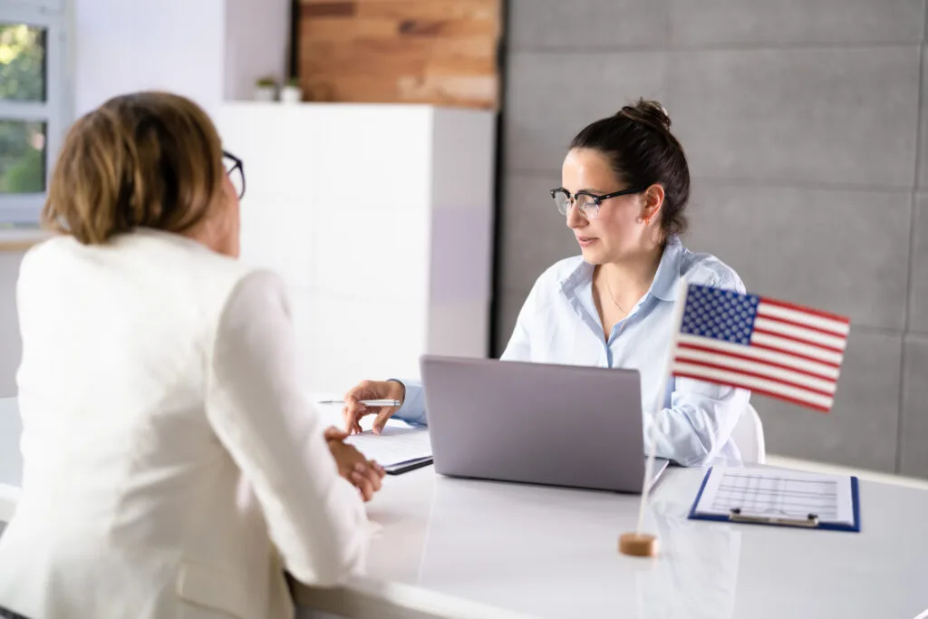 Imigracao eua atendimento visto casv Funcionária em um atendimento para solicitação de visto americano com bandeira dos estados unidos sobre a mesa.