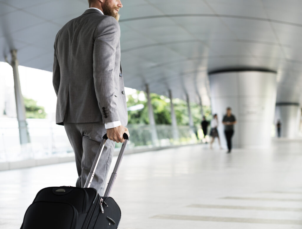 Businessman holding luggage business trip Homem de terno cinza puxando mala preta em corredor de aeroporto moderno