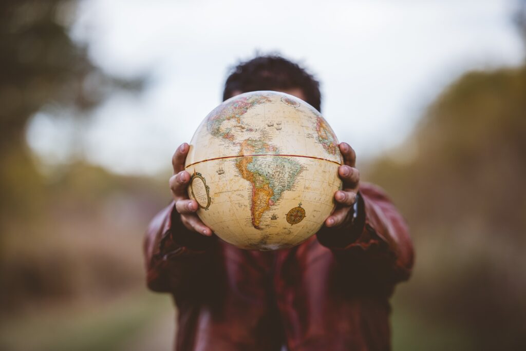 Closeup shot male wearing leather jacket holding globe front him Homem de jaqueta vermelha segurando globo terrestre vintage com américa do sul em destaque